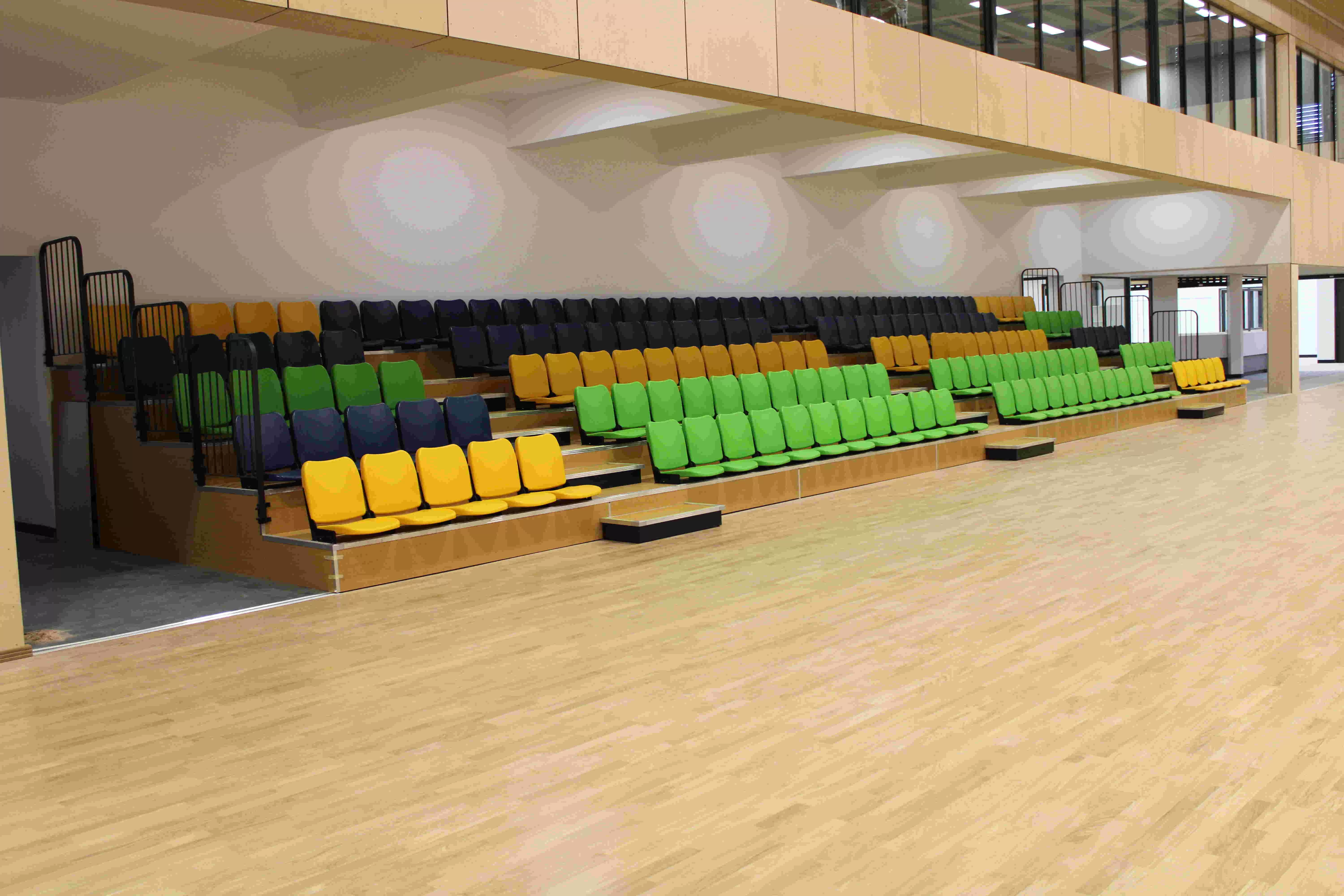 "Indoor fixed bleachers with wooden-look flooring, colorful seats (yellow, green, blue), and a metal structure base featuring fully enclosed treads and backrests."
