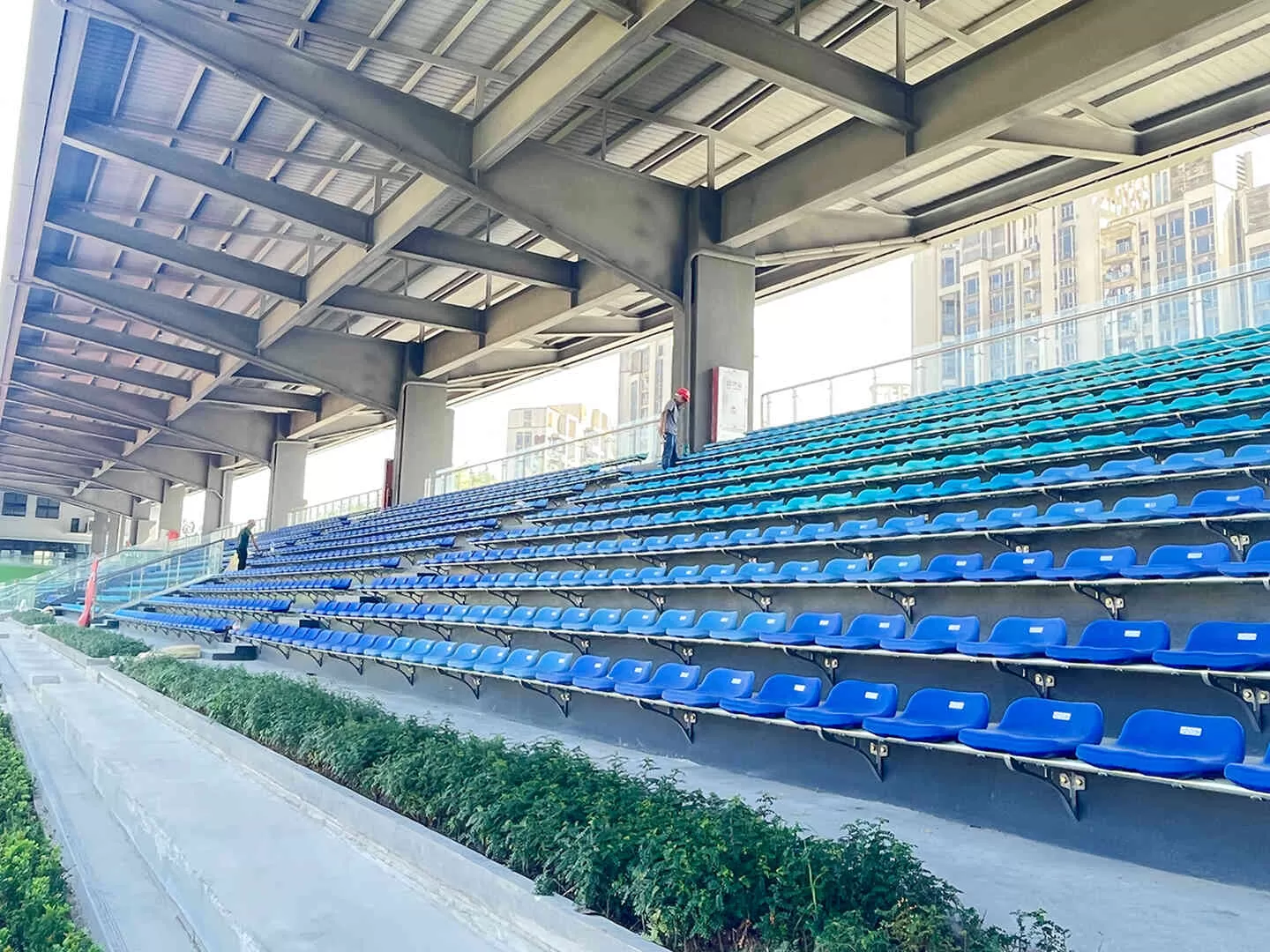 Blue Spoon-L integrated low-back stadium seats installed at Shenzhen Honghua Mountain Sports Center, with steel canopy structure and urban buildings in background