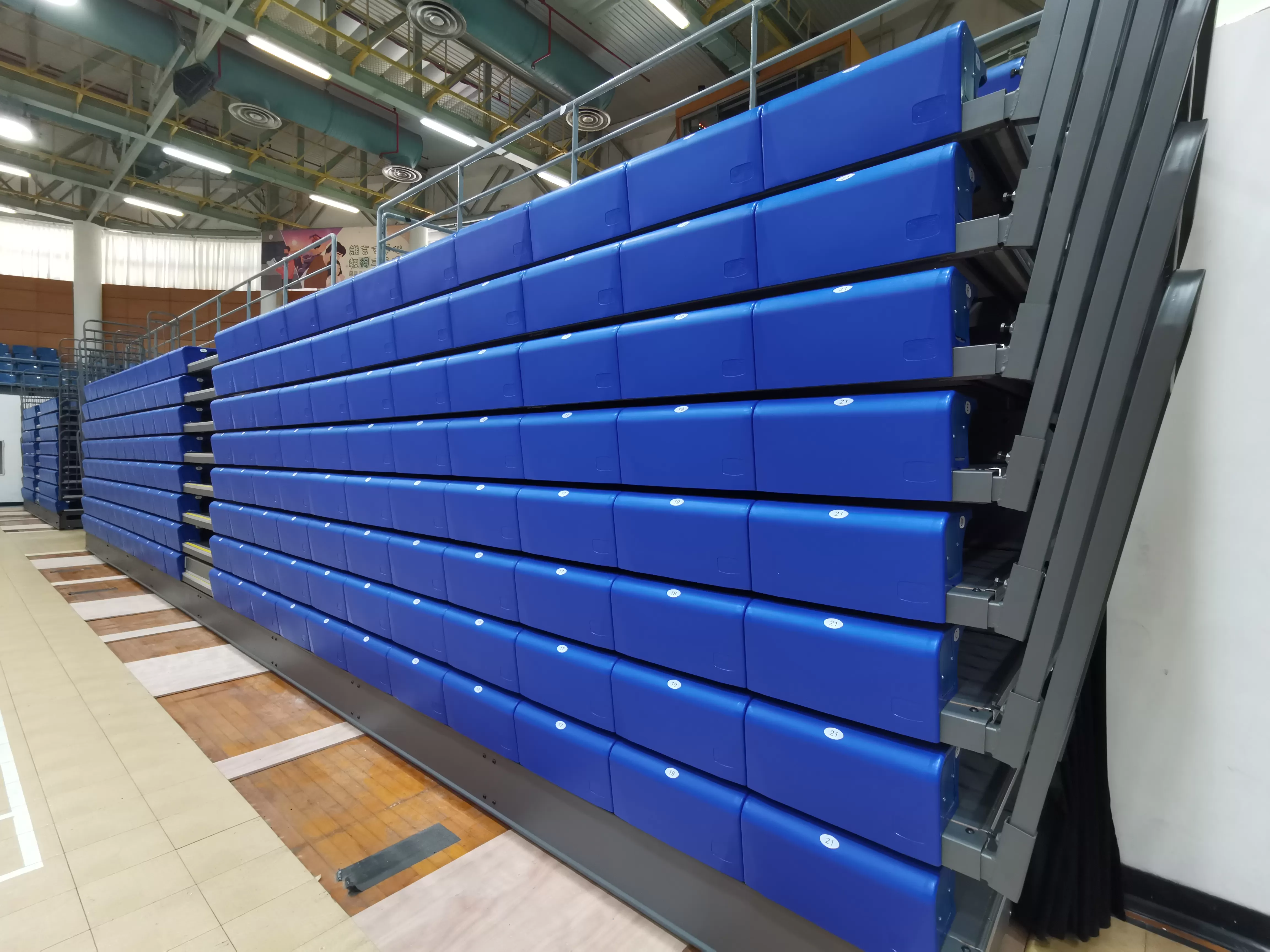 Stacked folded telescopic bleachers with blue HDPE gym spectator seats, compact retractable stands foldable bleachers portable grandstand for indoor arena sports hall grandstand at Macau Yuet Wah College indoor stadium